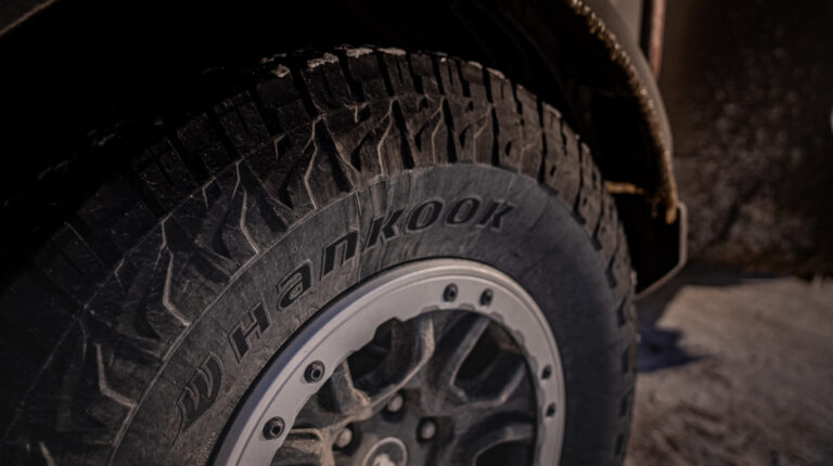 The new Hankook Dynapro AT2 Xtreme tire shown fitted to a vehicle with mud between the grooves and the brand name written on the sidewall.