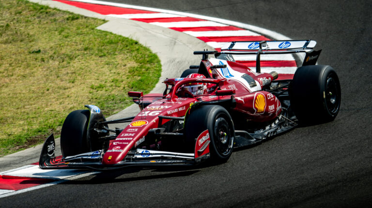 A red Formula 1 car takes a turn on a motorsport racetrack at high speed