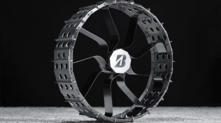 A wheel for a lunar rover shown in profile on a grey floor with a black background