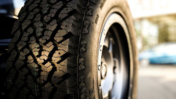 A close up of a tire fitted to a parked vehicle with the street and buildings appearing behind