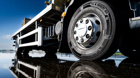 Close-up of a new Michelin truck tires for last-mile delivery fitted in a truck on a tarmac road, with the empty lane behind and blue sky above