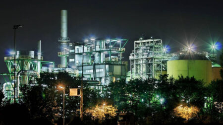 A Birla Carbon plant at night-time, with a range of lights and buildings alongside a tall chimney.