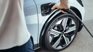 The Michelin Pilot Sport 5 Energy tire on a silver vehicle, which is being filled with fuel at a petrol station. The driver's arms and torso are partially visible.